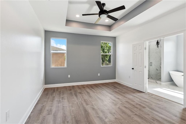 unfurnished bedroom with a tray ceiling, multiple windows, and baseboards