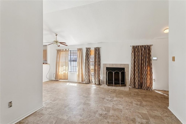 unfurnished living room with a tile fireplace, stone finish flooring, ceiling fan, and baseboards