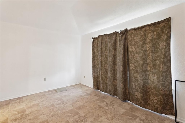 empty room featuring vaulted ceiling and baseboards