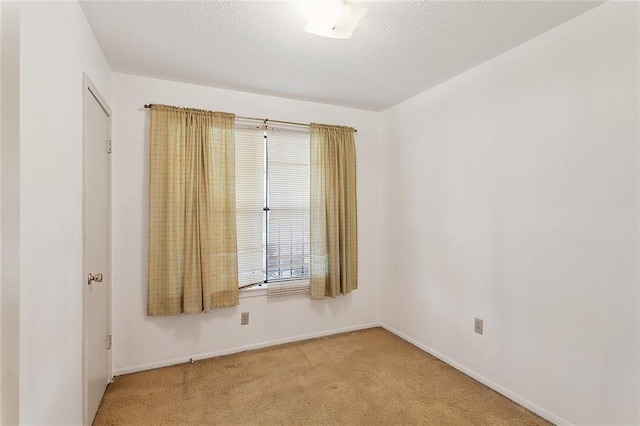 spare room with light carpet, baseboards, and a textured ceiling