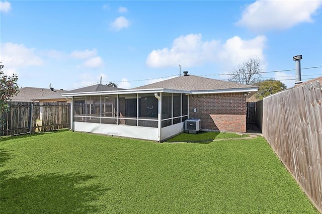 rear view of house featuring a sunroom, brick siding, a lawn, and a fenced backyard