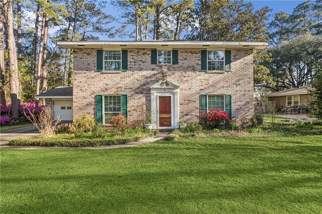 colonial inspired home featuring a garage, a front lawn, a chimney, and brick siding