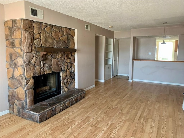 unfurnished living room featuring a textured ceiling, a fireplace, wood finished floors, and visible vents