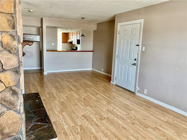 unfurnished living room with light wood-style flooring, baseboards, and a textured ceiling