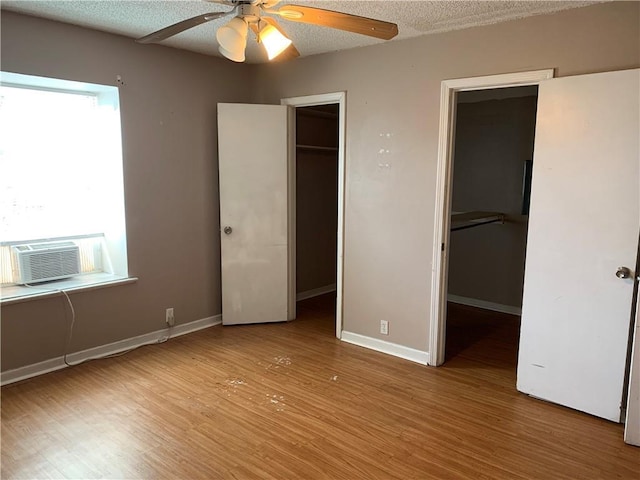 unfurnished bedroom with a walk in closet, a textured ceiling, wood finished floors, cooling unit, and baseboards