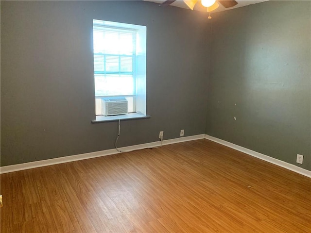 spare room with a ceiling fan, cooling unit, baseboards, and wood finished floors