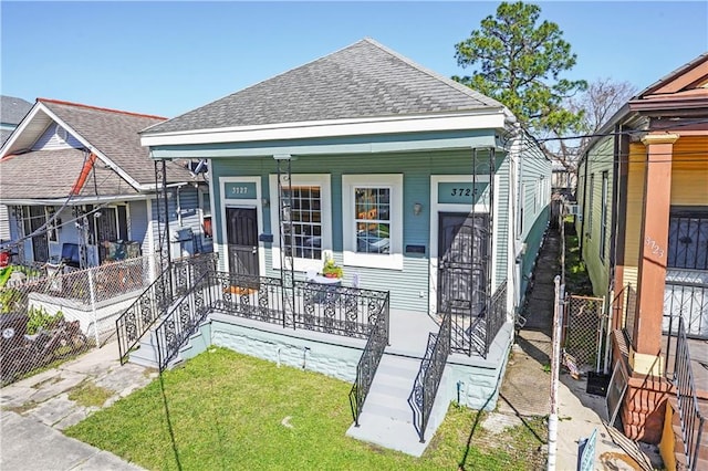 shotgun-style home featuring fence, covered porch, a front yard, and a shingled roof