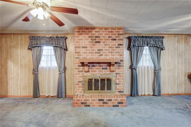 unfurnished living room featuring baseboards, ceiling fan, carpet floors, wood walls, and a fireplace