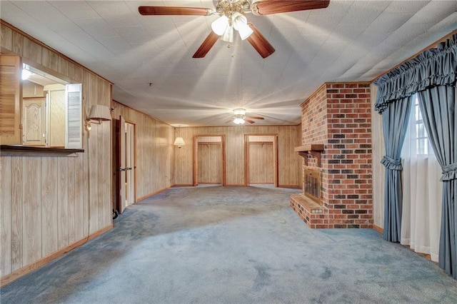 unfurnished living room featuring baseboards, a ceiling fan, wood walls, carpet floors, and a brick fireplace