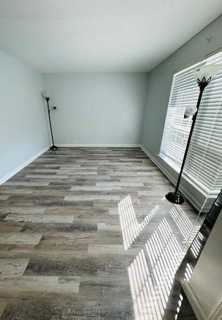 empty room with a textured ceiling, baseboards, and wood finished floors