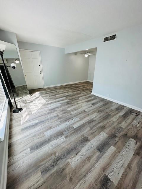 empty room with a ceiling fan, baseboards, visible vents, and wood finished floors