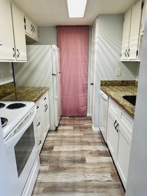 kitchen featuring white appliances, dark stone counters, light wood-style floors, white cabinetry, and a sink