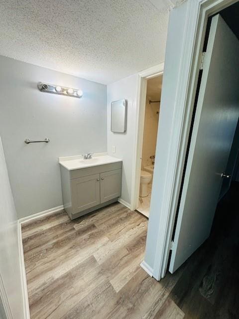 bathroom with toilet, vanity, a textured ceiling, wood finished floors, and baseboards