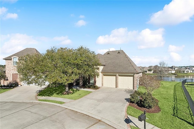 view of front of home with roof with shingles, a water view, an attached garage, a front yard, and driveway