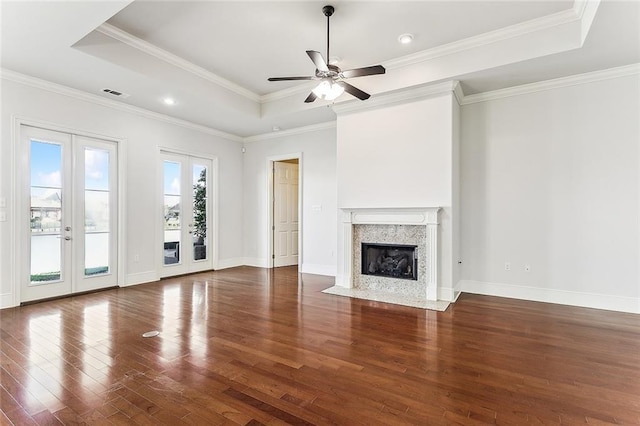 unfurnished living room with visible vents, wood finished floors, a tray ceiling, french doors, and a high end fireplace