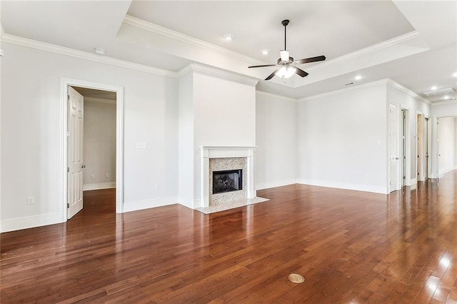 unfurnished living room featuring hardwood / wood-style flooring, a premium fireplace, a ceiling fan, baseboards, and a raised ceiling