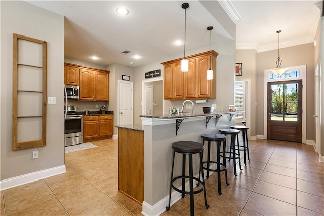 kitchen with light tile patterned floors, a peninsula, a breakfast bar, appliances with stainless steel finishes, and brown cabinets