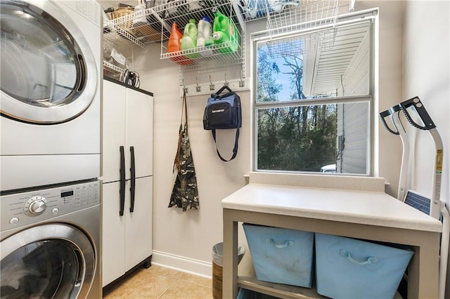 clothes washing area featuring stacked washer and dryer, cabinet space, baseboards, and light tile patterned floors