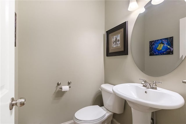 half bathroom with baseboards, a sink, and toilet