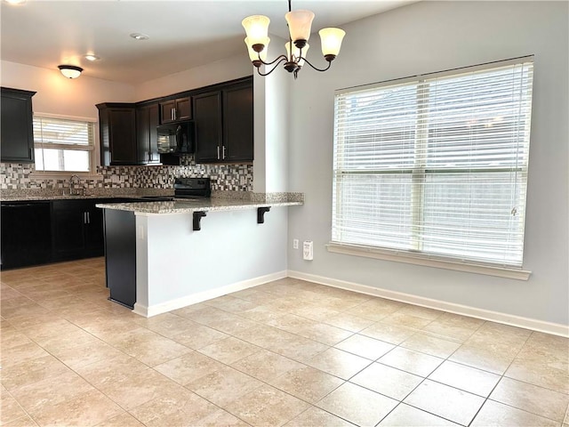 kitchen with black appliances, light stone counters, backsplash, and a kitchen breakfast bar