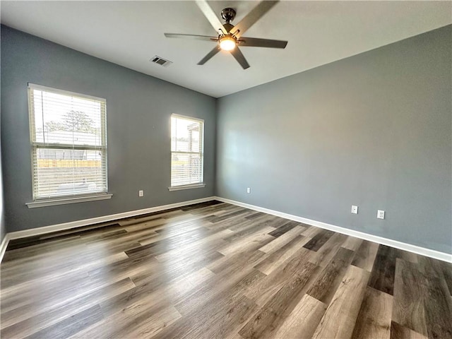 spare room with dark wood-style floors, visible vents, ceiling fan, and baseboards