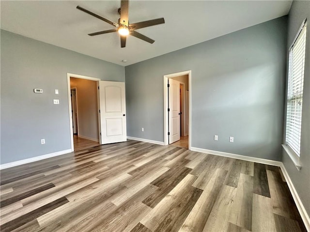 unfurnished bedroom with ceiling fan, multiple windows, wood finished floors, and baseboards