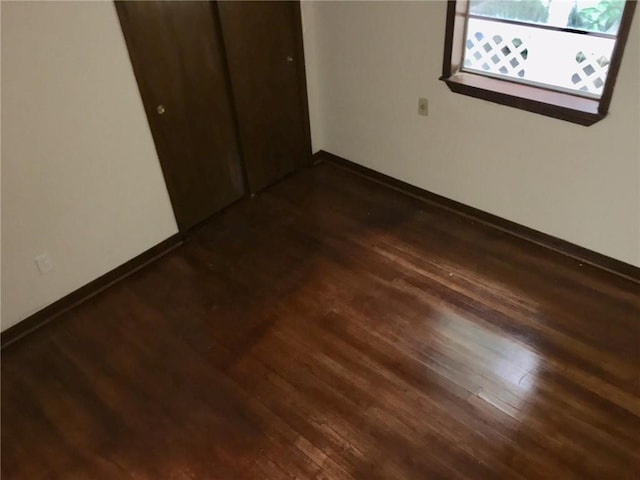 unfurnished bedroom featuring a closet, dark wood finished floors, and baseboards