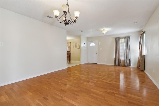 interior space with a textured ceiling, visible vents, baseboards, light wood finished floors, and an inviting chandelier