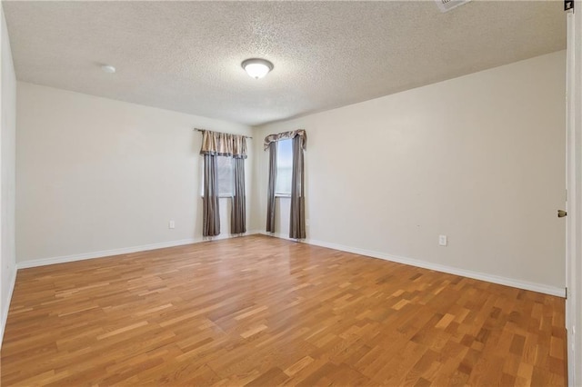 empty room featuring a textured ceiling, light wood finished floors, and baseboards