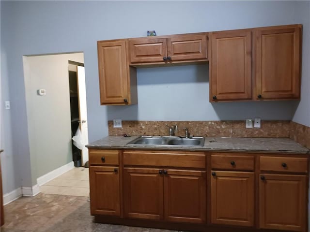 kitchen featuring dark countertops, baseboards, brown cabinets, and a sink