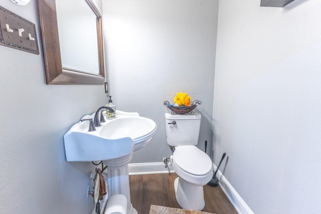 half bathroom featuring a sink, toilet, baseboards, and wood finished floors