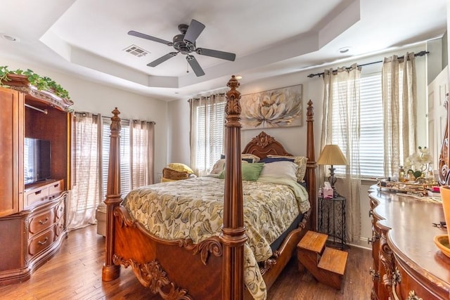 bedroom featuring ceiling fan, visible vents, a raised ceiling, and wood finished floors