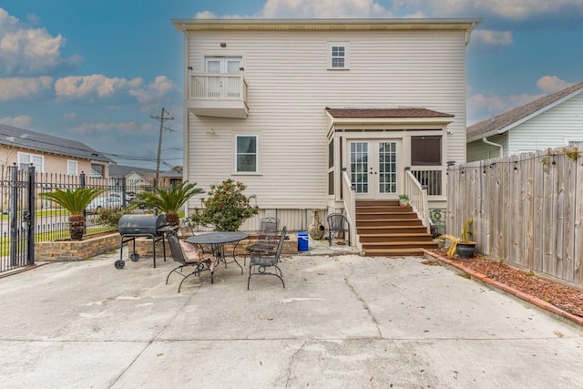 back of property with a balcony, a fenced backyard, a patio, and french doors