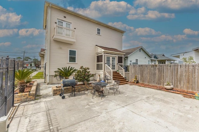 rear view of house featuring a patio, french doors, fence, and a balcony