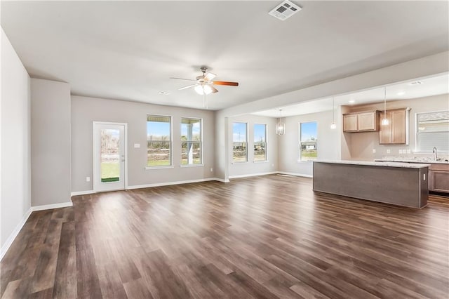 unfurnished living room with dark wood-style flooring, visible vents, a ceiling fan, a sink, and baseboards