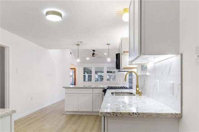 kitchen with a sink, decorative light fixtures, backsplash, light wood-style floors, and light stone countertops