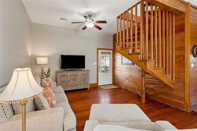 living room with wooden walls, visible vents, a ceiling fan, wood-type flooring, and stairway