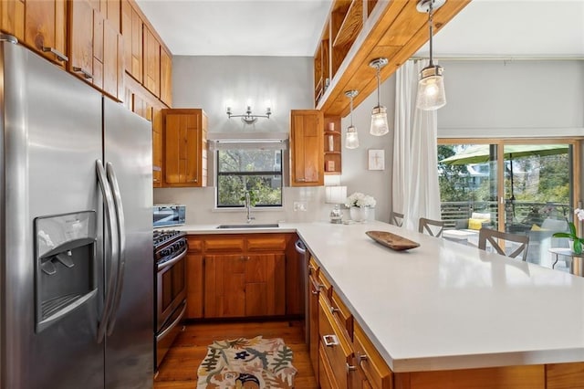 kitchen with brown cabinetry, appliances with stainless steel finishes, a peninsula, light countertops, and a sink