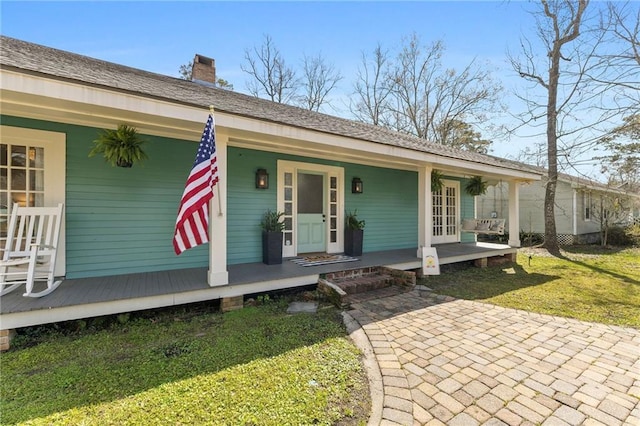 view of front of property with a shingled roof, covered porch, a chimney, and a front lawn