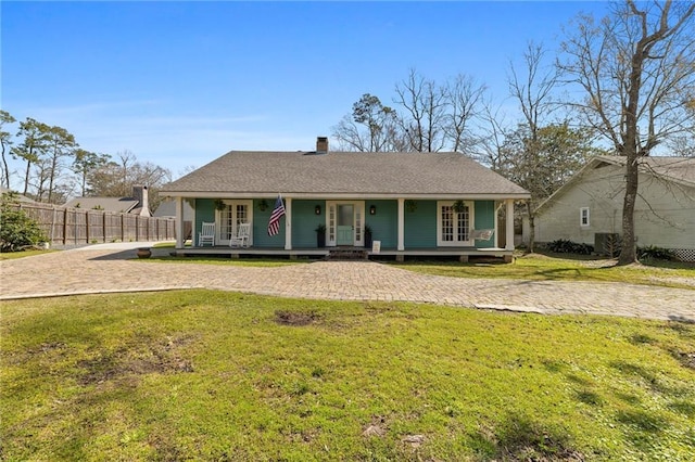 view of front facade with french doors, a front lawn, a porch, and fence