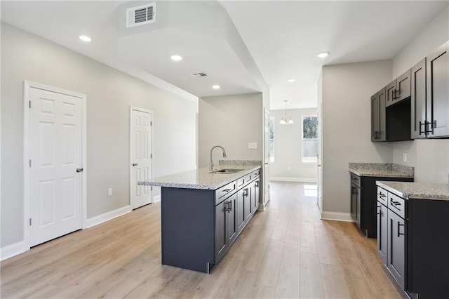 kitchen featuring light stone counters, visible vents, light wood finished floors, and a sink