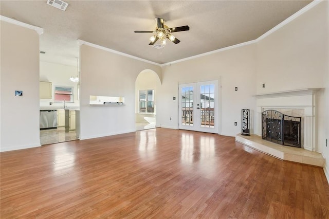 unfurnished living room with a fireplace with raised hearth, visible vents, french doors, light wood-type flooring, and crown molding