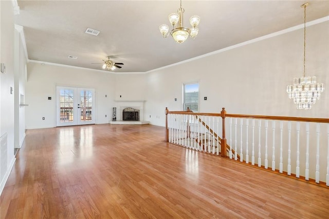 unfurnished living room with visible vents, a fireplace with raised hearth, wood finished floors, crown molding, and ceiling fan with notable chandelier