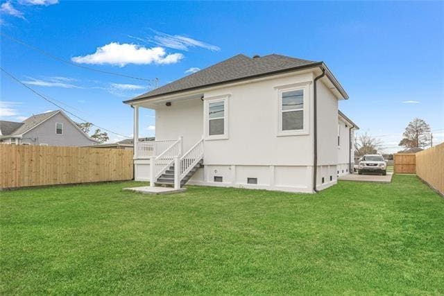 rear view of property featuring crawl space, a fenced backyard, a lawn, and stucco siding