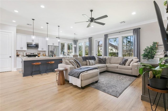 living area with light wood-style floors, visible vents, and crown molding