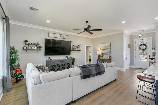 living room featuring light wood-style floors, baseboards, visible vents, and crown molding