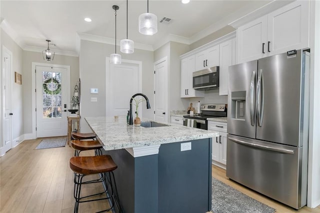 kitchen featuring visible vents, an island with sink, appliances with stainless steel finishes, ornamental molding, and a sink