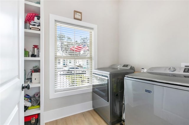 clothes washing area with light wood finished floors, laundry area, a healthy amount of sunlight, and washer and dryer