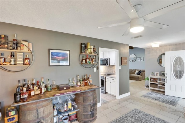 bar featuring ceiling fan, light tile patterned floors, a textured ceiling, stainless steel appliances, and visible vents