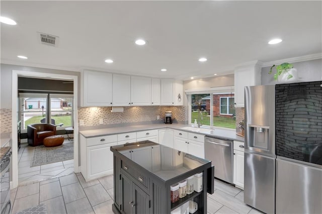 kitchen featuring white cabinets, appliances with stainless steel finishes, backsplash, a healthy amount of sunlight, and a sink